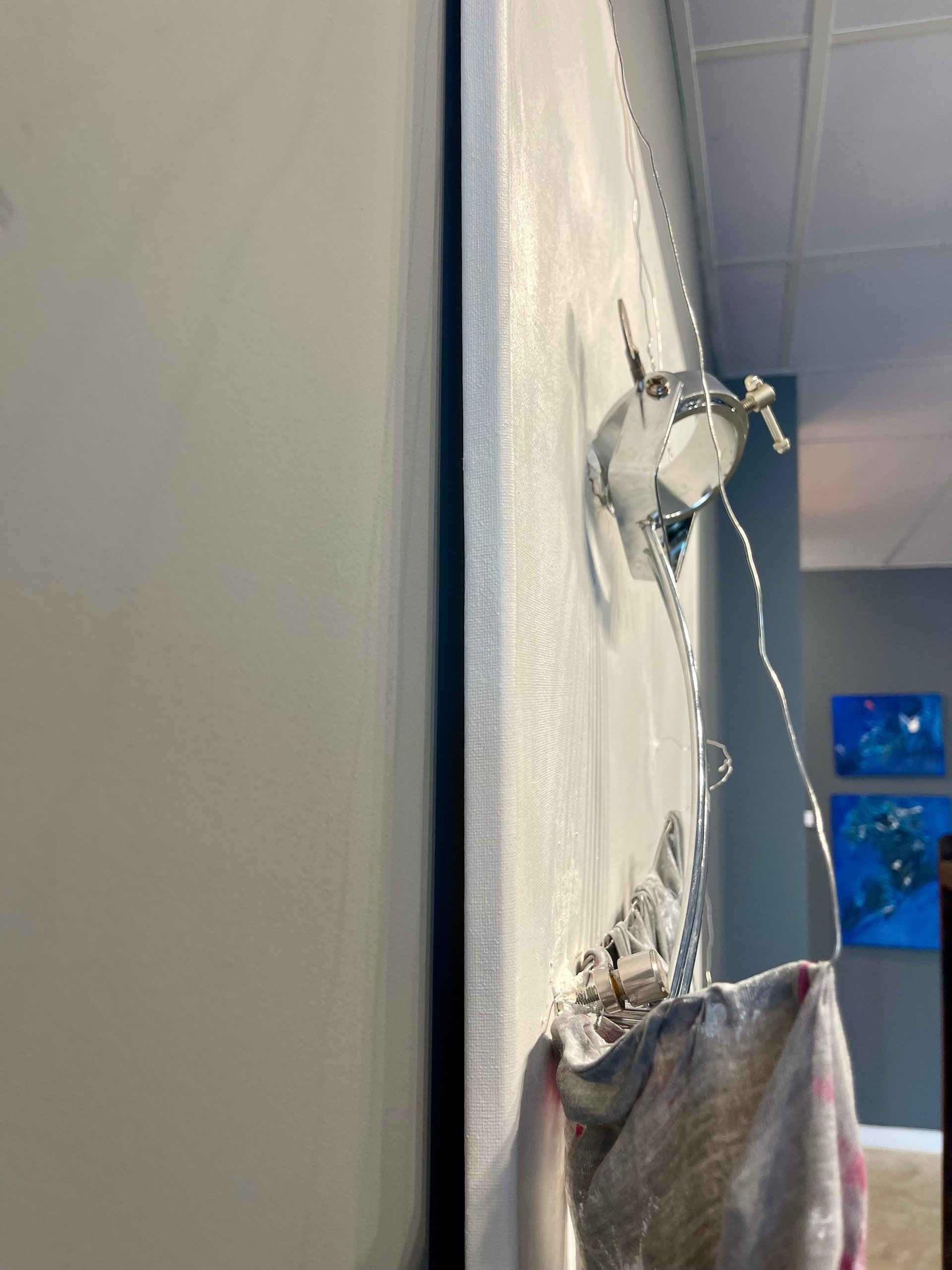 Wall-mounted electrical outlet with exposed wiring and cloth material hanging below, mounted on a light-colored interior wall