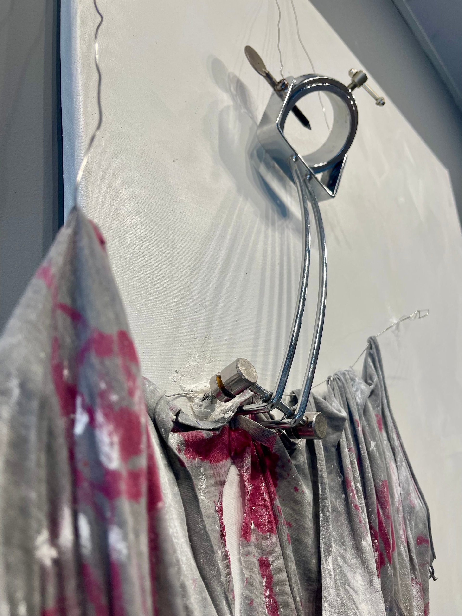 Stainless steel shower head mounted on white tiled wall with pink and white tie-dye patterned fabric hanging below